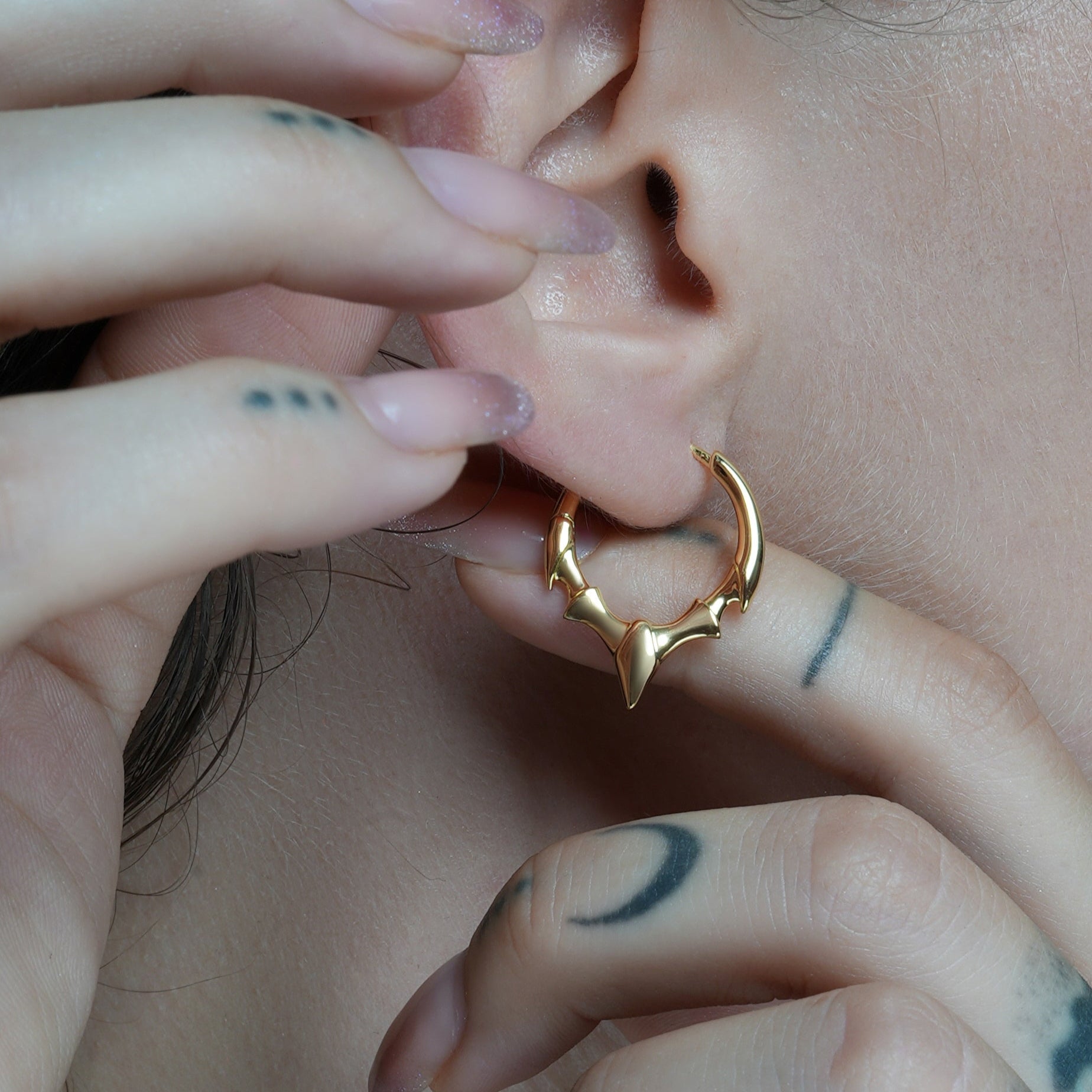 Close-up of a gold-tone fang crest hoop earring on model's ear with hand near face