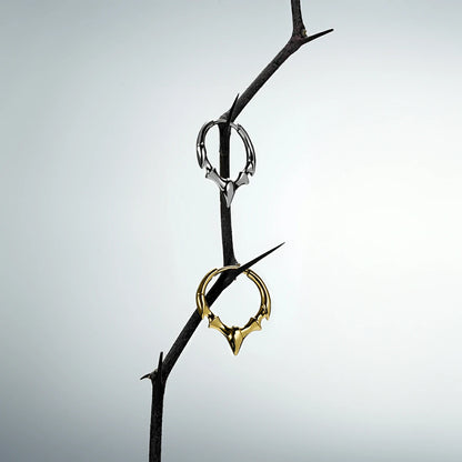 Silver and gold Fang Crest hoop earrings hanging from a dark thorn branch