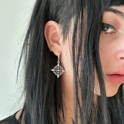 Fleur-de-Lis Elegance Earrings in 925 sterling silver, worn in a close portrait with long black face-framing hair and a black