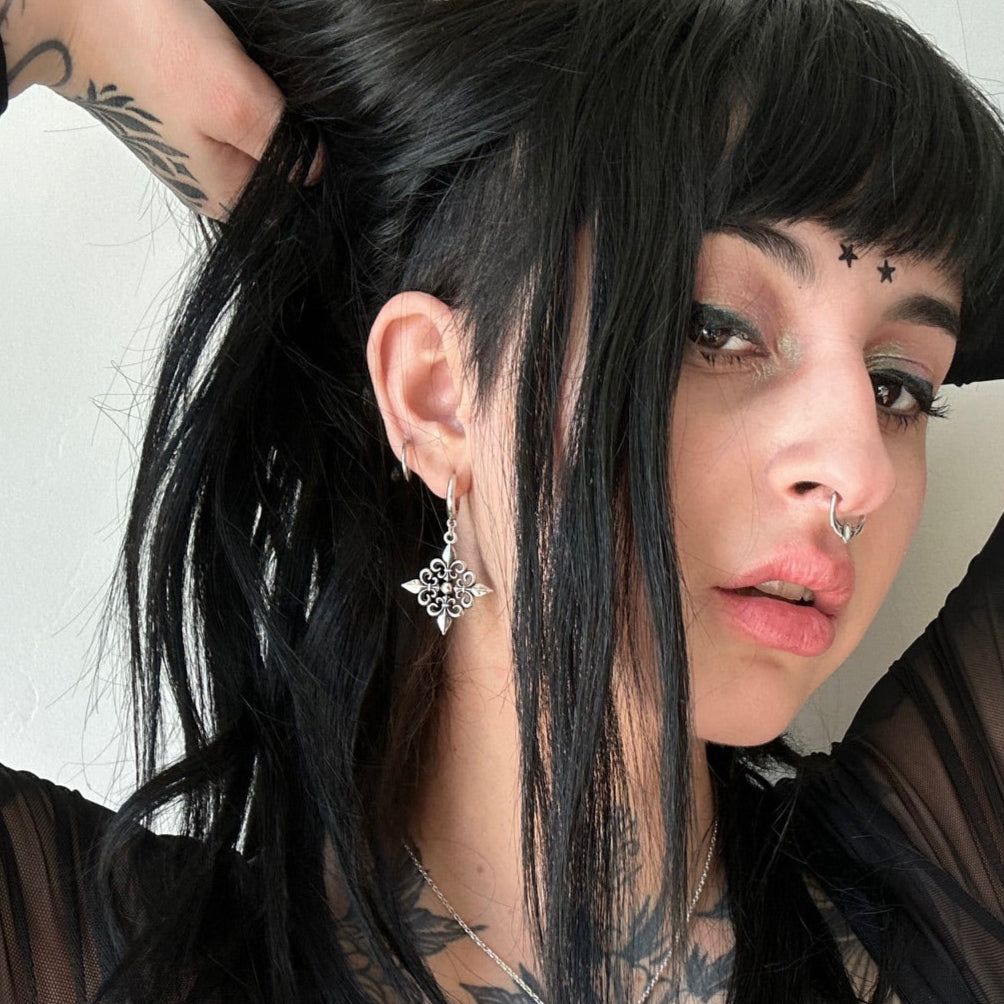 Fleur-de-Lis Elegance Earrings in 925 sterling silver, worn in a selfie with black shag hair, facial piercings, and a raised 