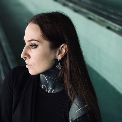 Fleur-de-Lis Elegance Earrings in 925 sterling silver, worn in side profile with a black turtleneck, neck tattoos, and a dark