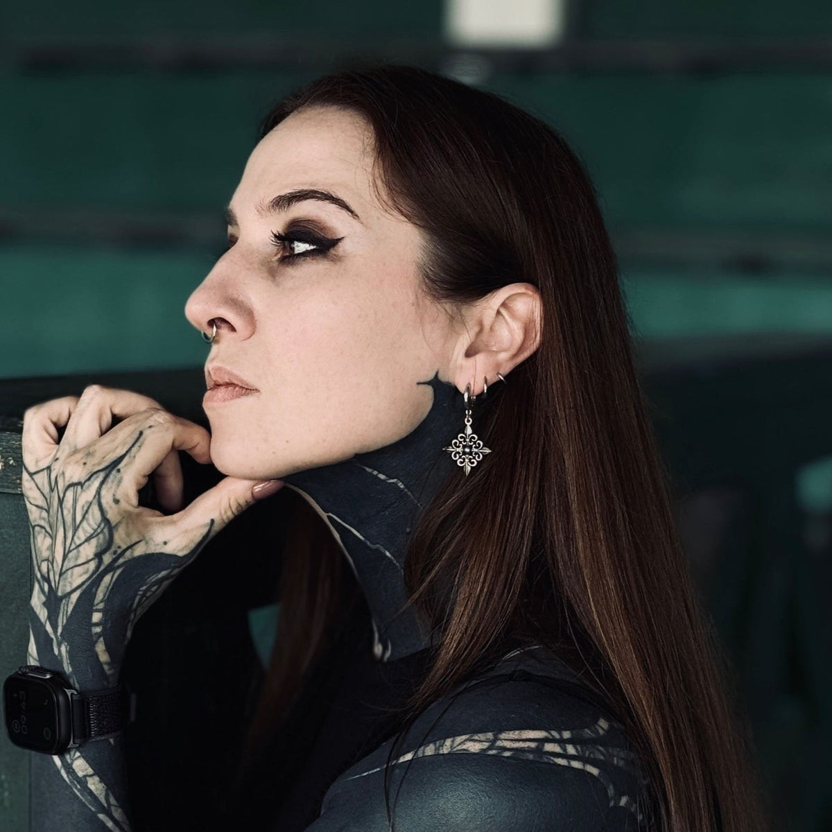 Fleur-de-Lis Elegance Earrings in 925 sterling silver, worn in side profile with brown hair, a black high neck top, and a tat