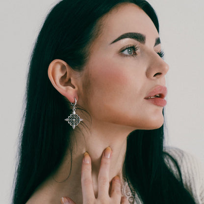 Fleur-de-Lis Elegance Earrings in 925 sterling silver, worn in side profile with dark green-black hair and a hand lightly tou