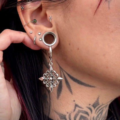 Silver-tone Fleur-de-Lis Elegance earring hanging through a circular ear tunnel in a layered piercing look