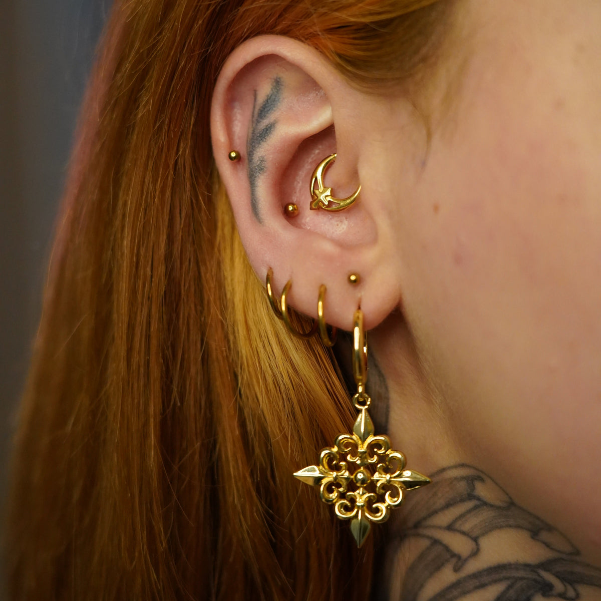 Gold-tone Fleur-de-Lis Elegance hoop earring worn in a layered ear stack with multiple small hoops