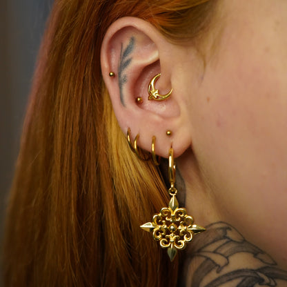 Gold-tone Fleur-de-Lis Elegance hoop earring worn in a layered ear stack with multiple small hoops