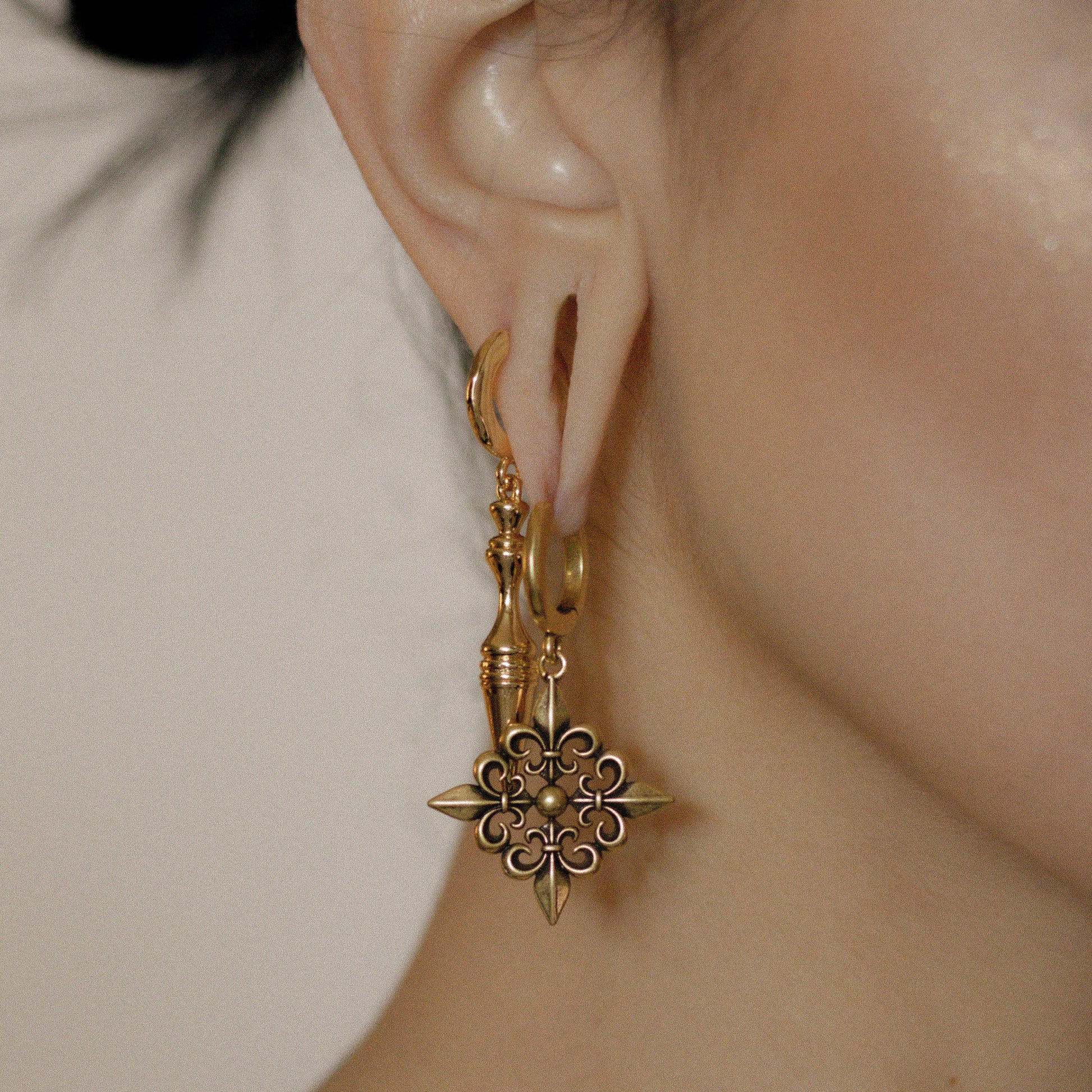 Gold-tone Fleur-de-Lis Elegance hoop earring worn in side profile beside a model's raised hand