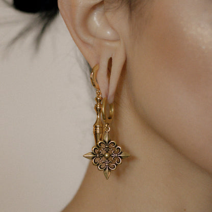 Gold-tone Fleur-de-Lis Elegance hoop earring worn in side profile beside a model's raised hand