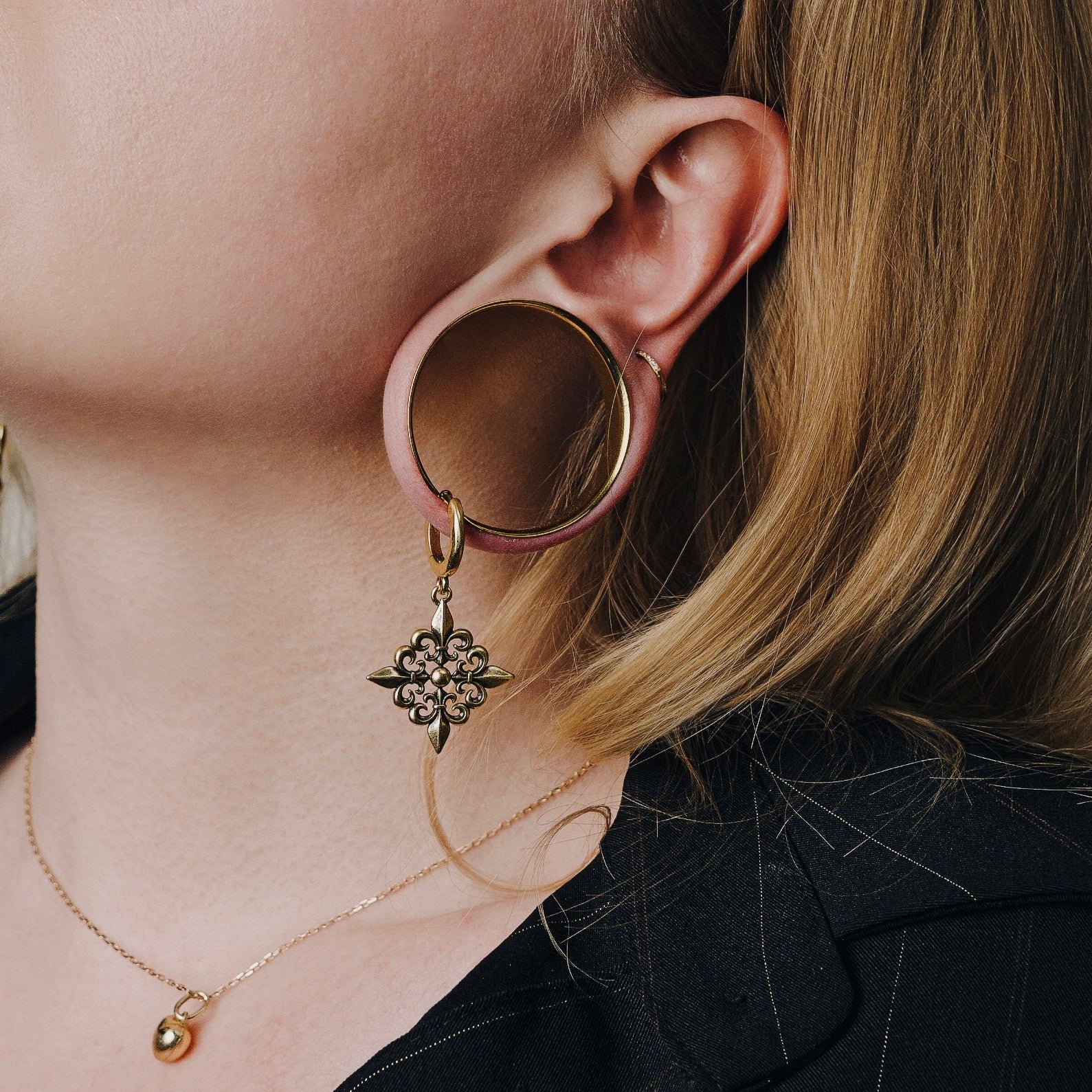Silver-tone Fleur-de-Lis Elegance earring hanging beneath a large circular ear plug