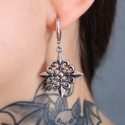 Close-up of a fleur-de-lis dangle earring in dark antiqued silver-tone worn on a model with a tattooed neck