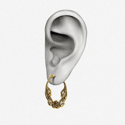 Close-up of an ear wearing a gold-tone floral scroll hoop earring with latch closure