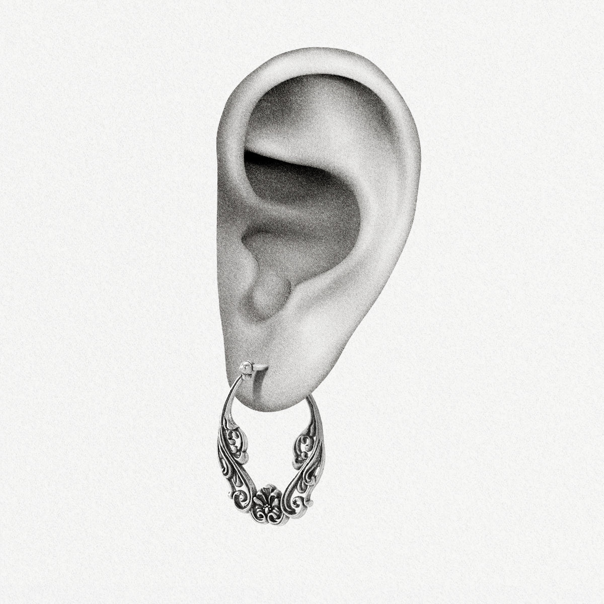 Close-up of an ear wearing a silver-tone floral scroll hoop earring with latch closure