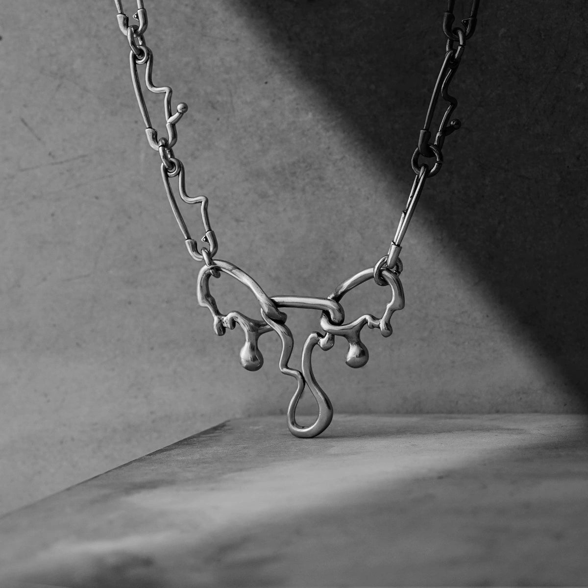 Silver Fluid Pin necklace draped over a concrete ledge