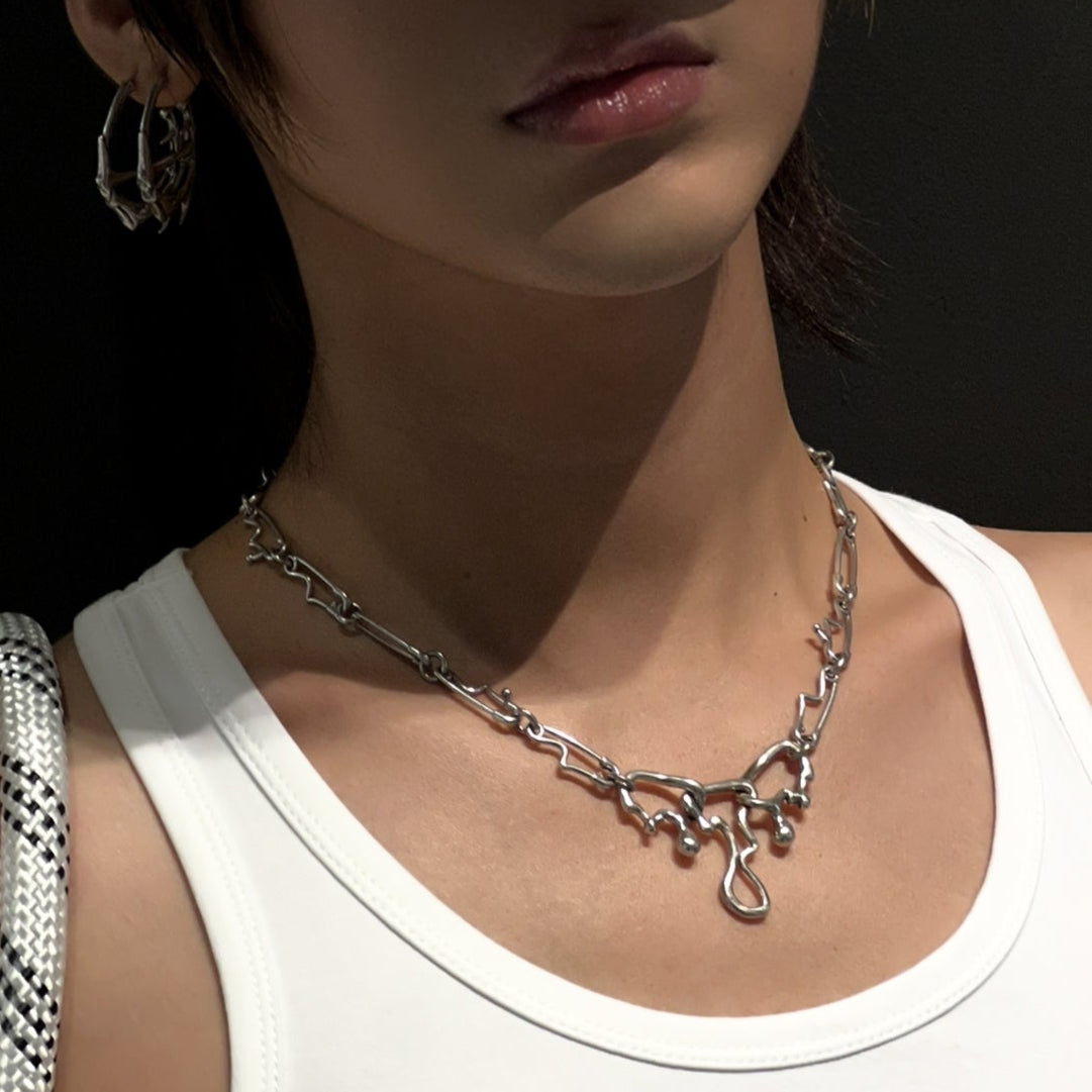 Silver-tone fluid pin necklace worn by a model with a hoop earring and white tank top, close-up