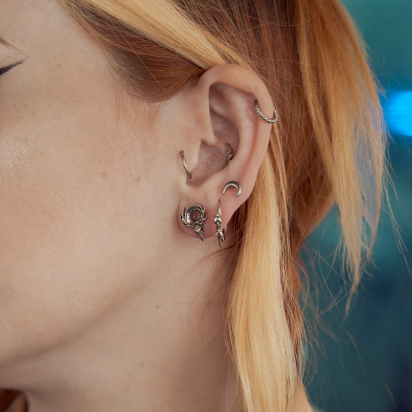 Model wearing a silver-tone deer skull hoop earring paired with crescent moon and cartilage studs
