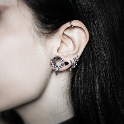 Model wearing a silver-tone deer skull hoop earring with antlers alongside small stud earrings