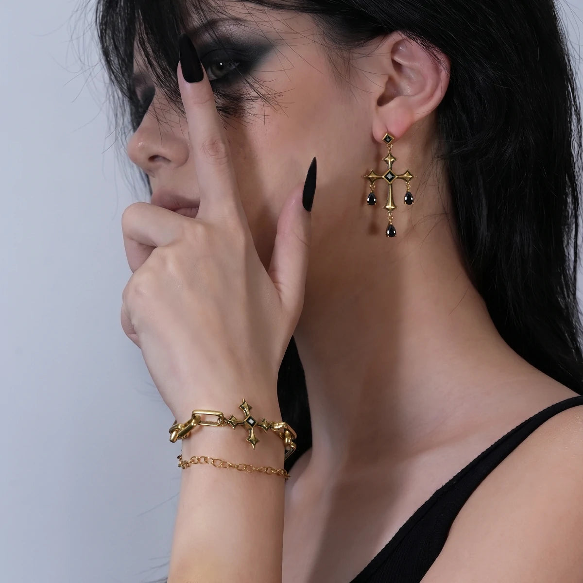 Forsaken Vow Earrings in antiqued 18K gold worn on the ear with a hand raised beside the cheek in a styling portrait.