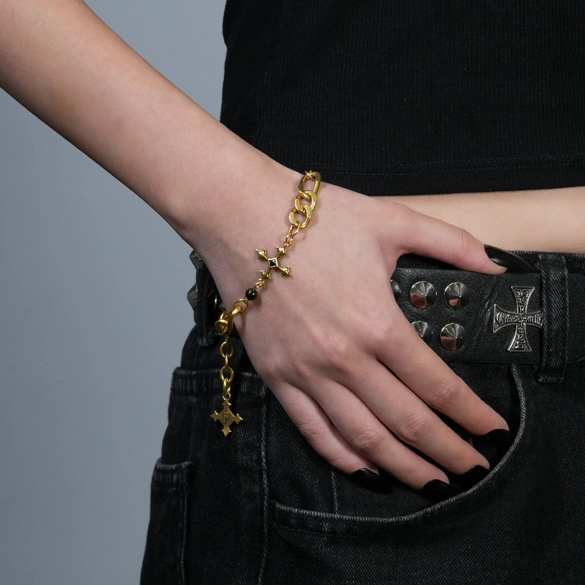 Fractured Creed Bracelet in antiqued 18K gold worn on the wrist with the hand resting at the hip over a black outfit.