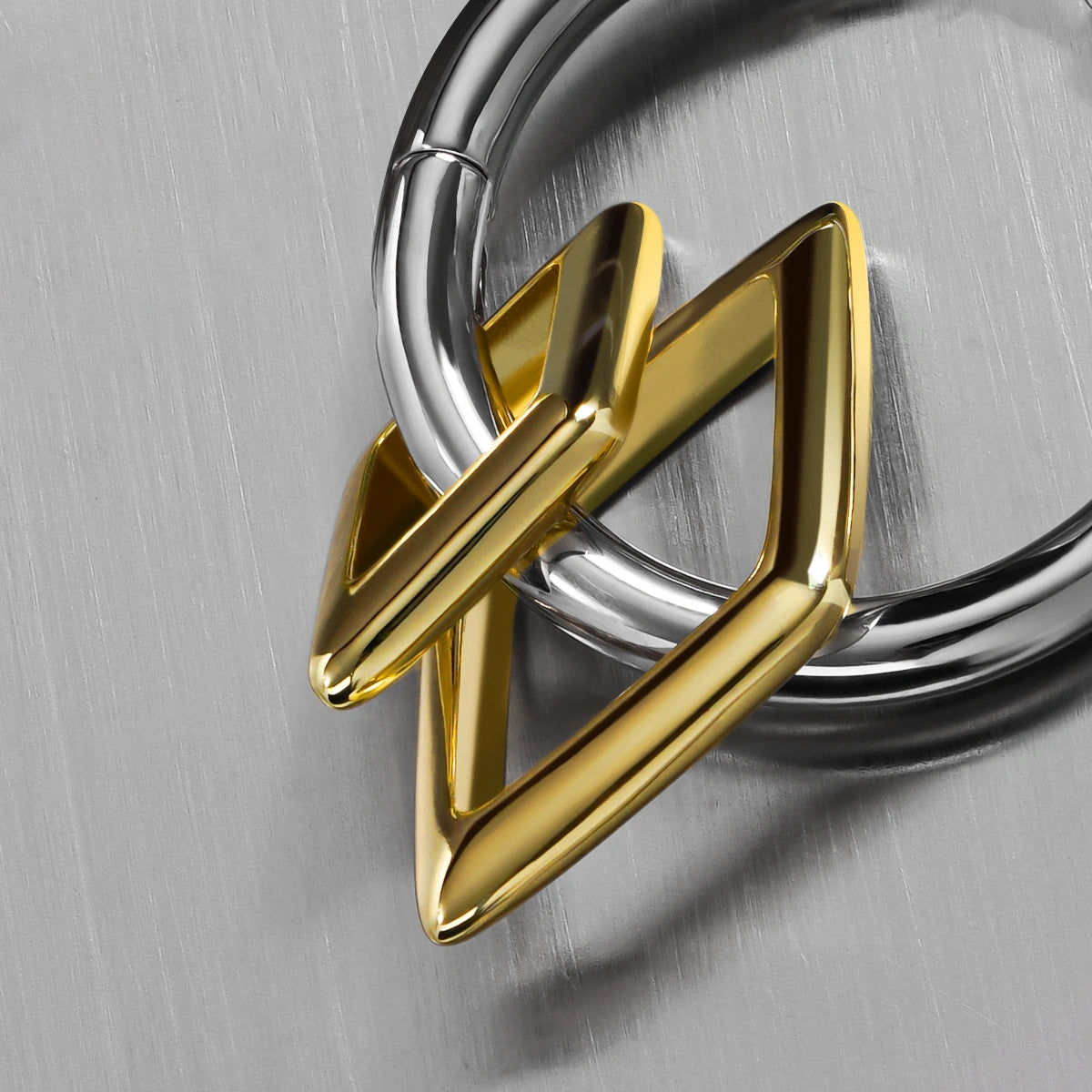 Close-up of a silver-tone hoop earring with a gold-tone geometric diamond charm, laid on a brushed metal surface