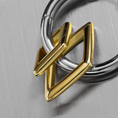 Close-up of a silver-tone hoop earring with a gold-tone geometric diamond charm, laid on a brushed metal surface