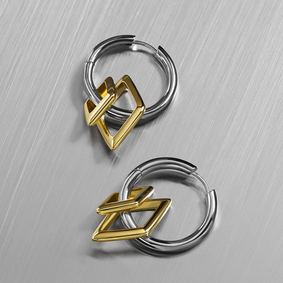 Pair of silver-tone hoop earrings with gold-tone diamond charms, arranged on a brushed metal surface