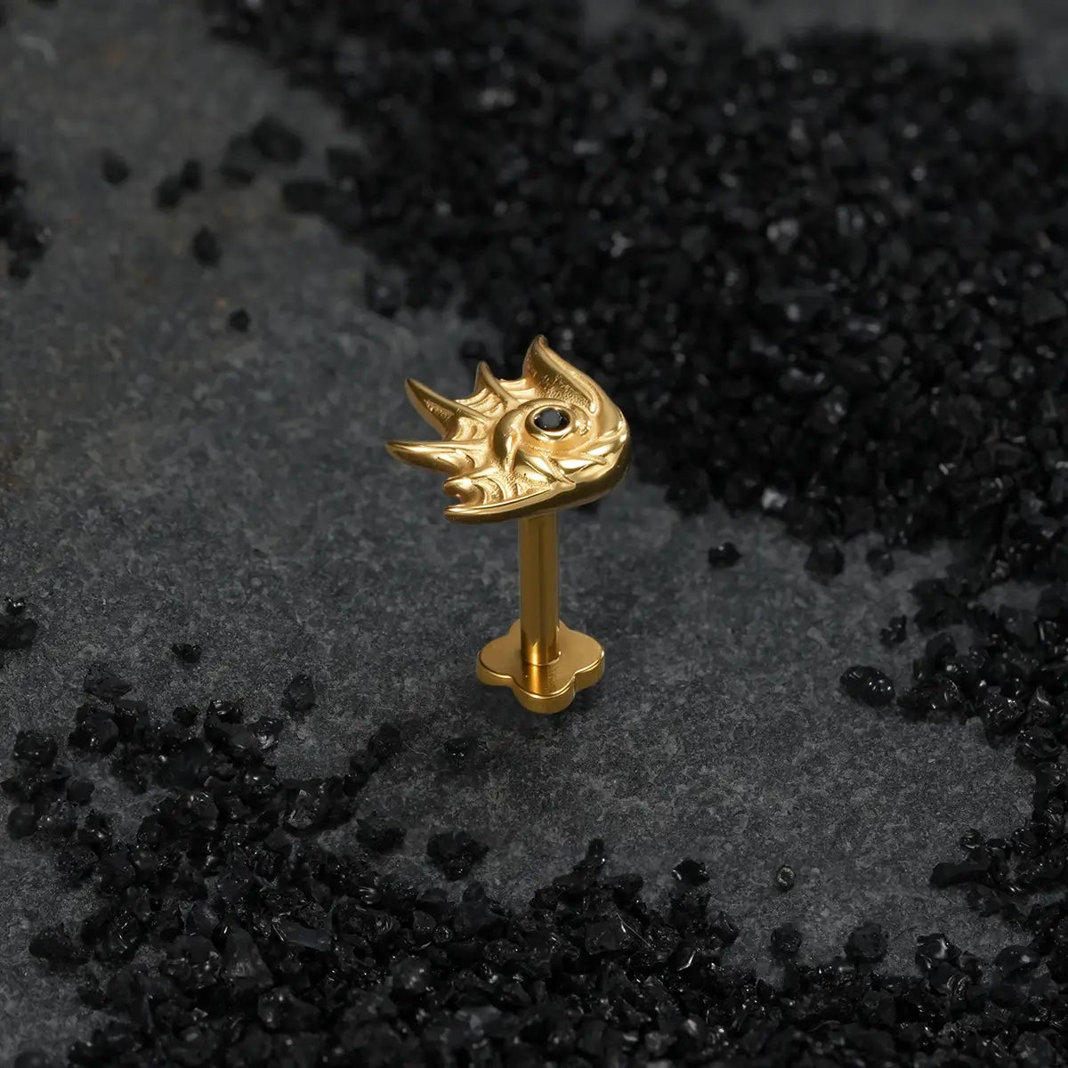 Gold sea creature conch ear stud with black stone center on dark background