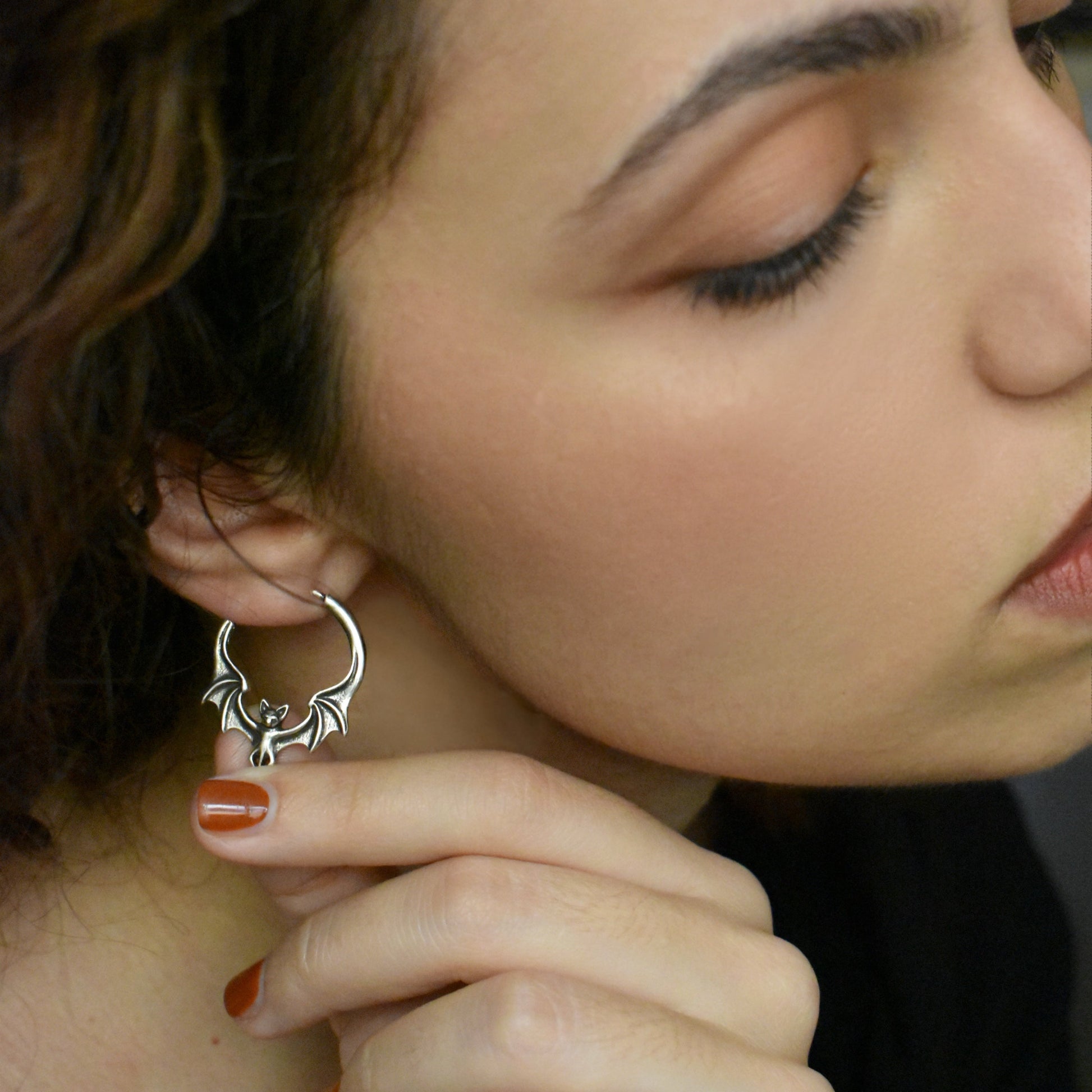 Model with dark curly hair wearing a silver bat-shaped hoop earring, close-up view