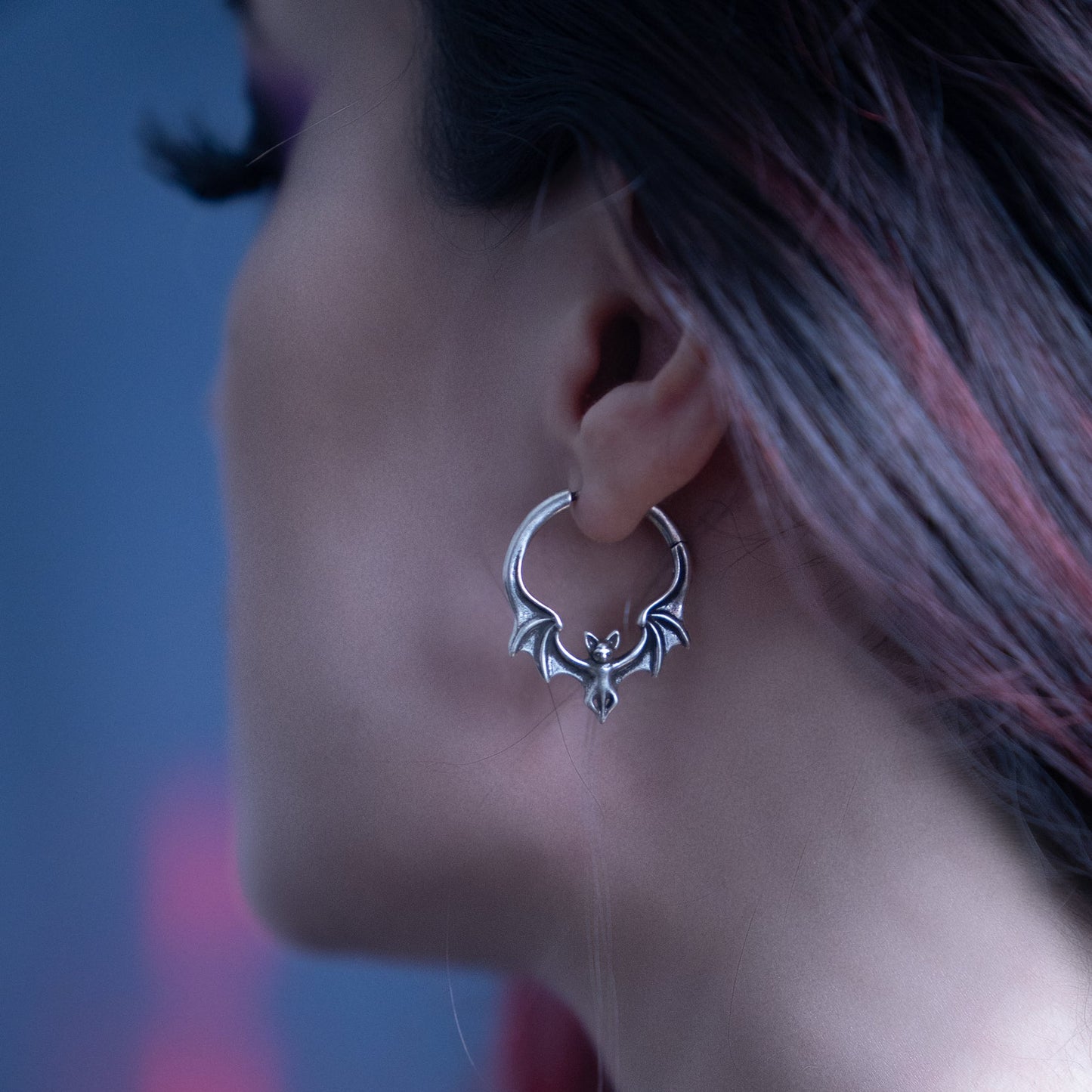 Silver-tone bat-shaped hoop earring worn on ear, profile view against blurred background