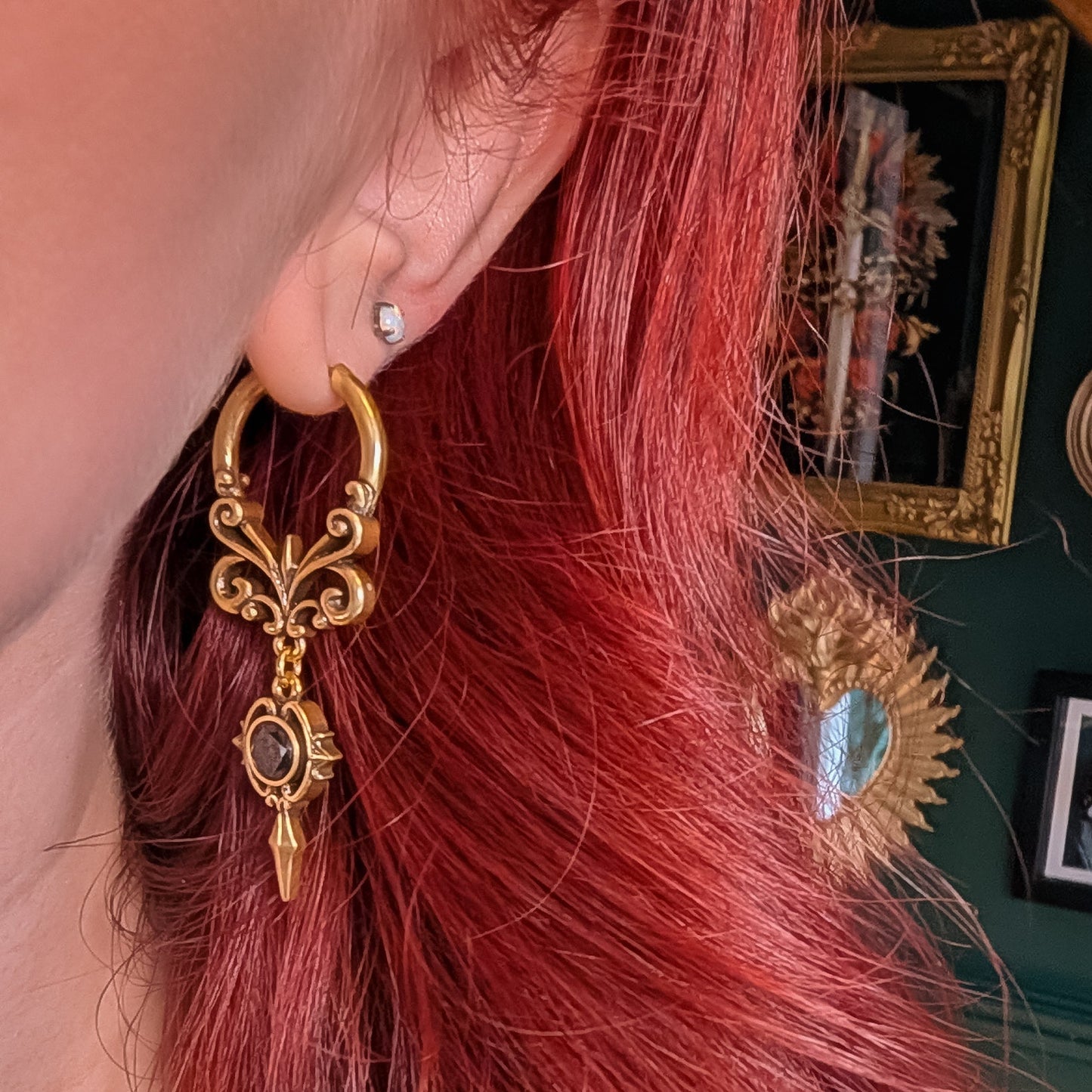 Gold-tone Gothic Crest hoop earring with a black oval stone worn against red hair in side profile