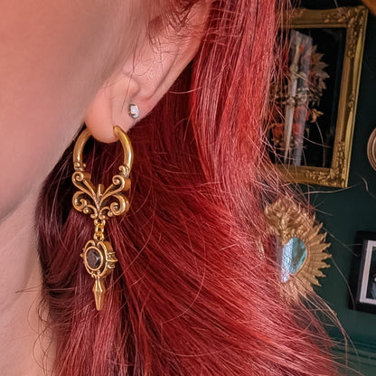 Gold-tone Gothic Crest hoop earring with a black oval stone worn against red hair in side profile