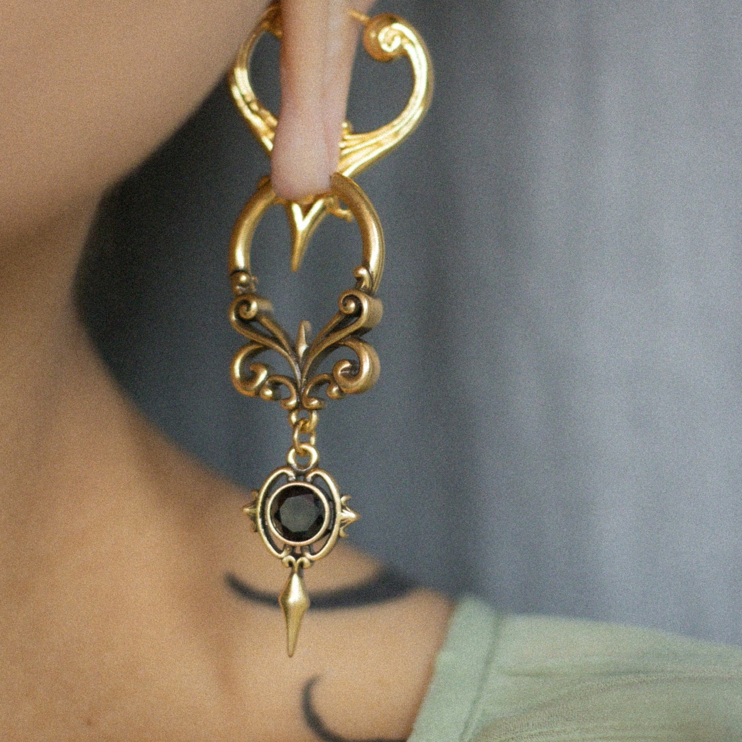 Close-up of a gold-tone Gothic Crest hoop earring with curled filigree and a black oval center stone