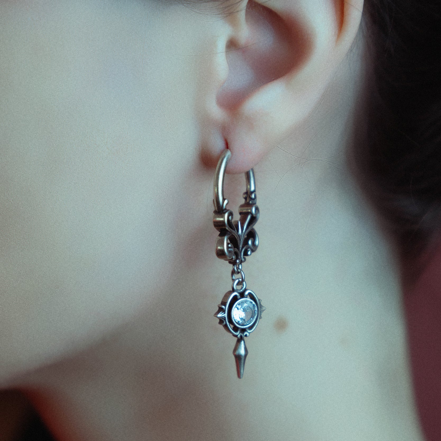 Silver-tone gothic crest earring worn on hoop with crystal charm and spike drop, close-up side view