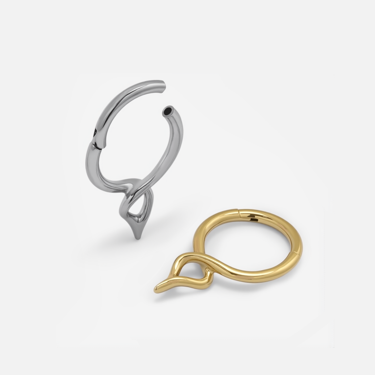 Silver-tone and gold-tone twist clicker rings with teardrop drops laid side by side, one open and one closed