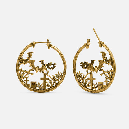 Gold-tone hoop earrings with bats, cross headstones, and RIP grave markers in a graveyard design