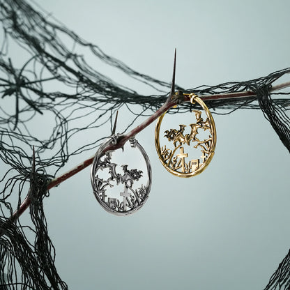Silver and gold Graveyard Bat hoop earrings hanging from a dark branch