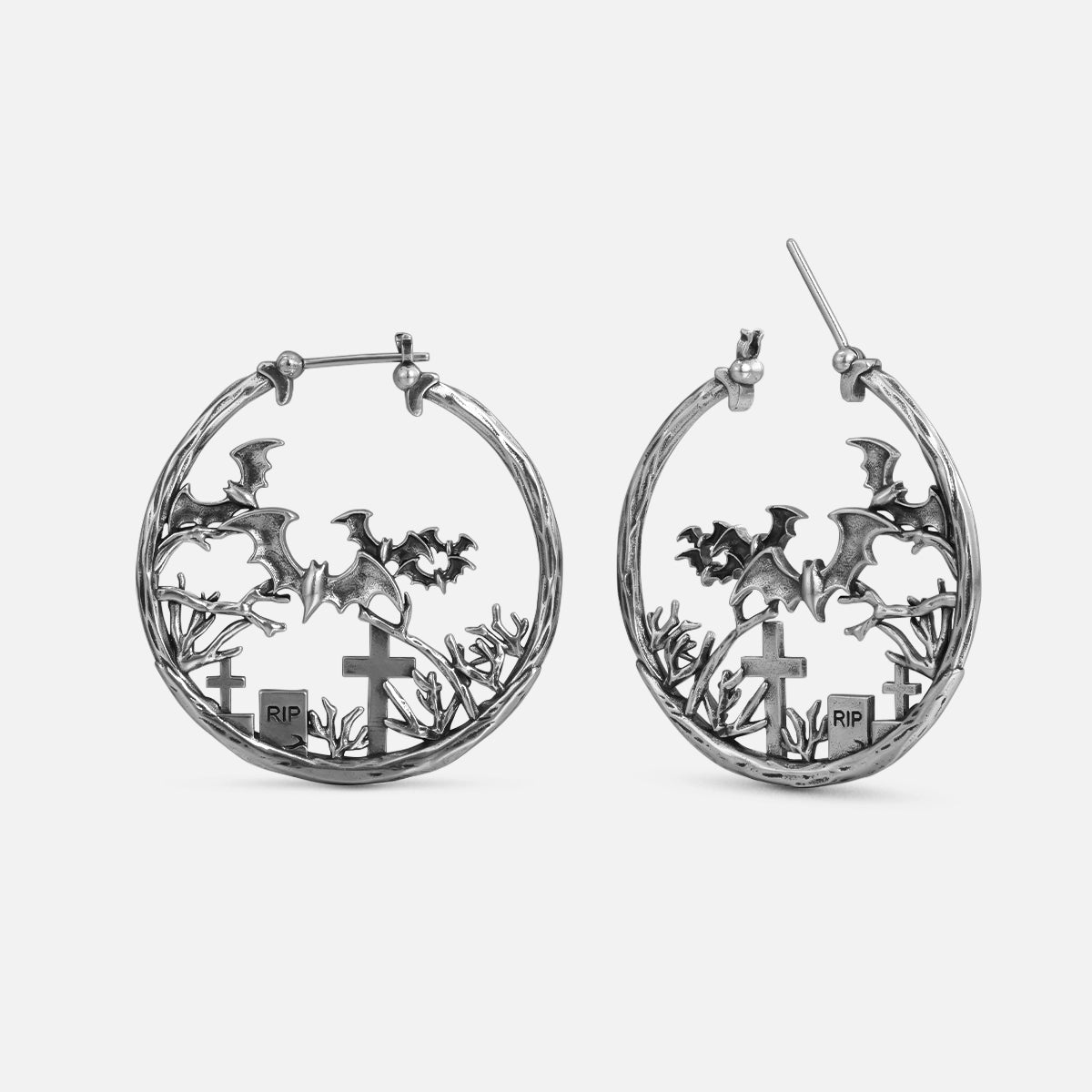 Silver-tone hoop earrings with bats, cross headstones, and RIP grave markers in a graveyard scene
