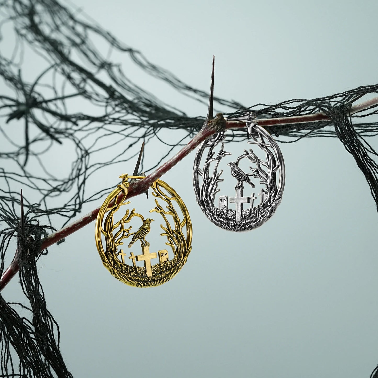 Silver and gold Graveyard Raven hoop earrings hanging from a dark branch