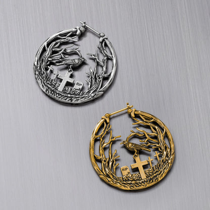 Silver-tone and gold-tone hoop earrings side by side, each featuring a raven and cross gravestones amid branches