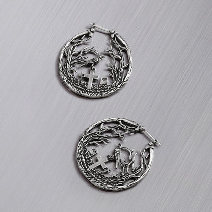 Pair of silver-tone hoop earrings with raven and cross gravestone details set within a branch motif, top view