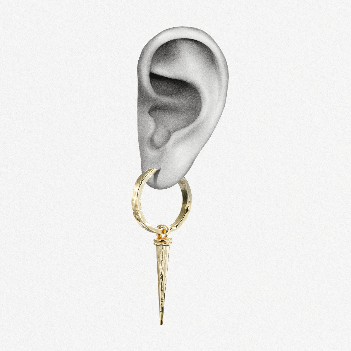 Close-up of an ear wearing a gold-tone hammered hoop earring with a tapered spike drop