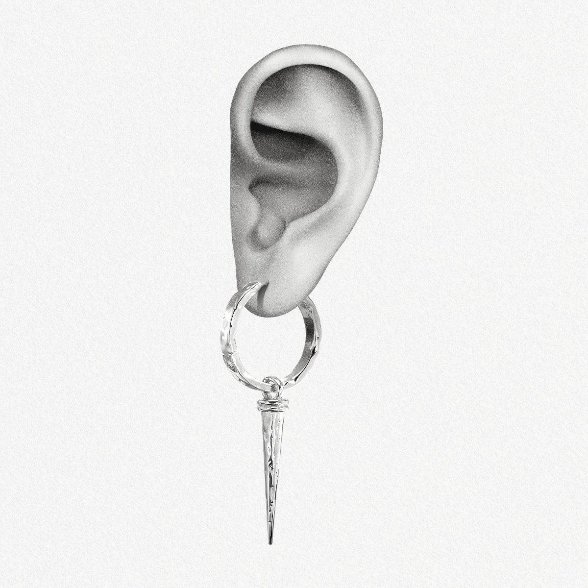 Close-up of an ear wearing a silver-tone hammered hoop earring with a tapered spike drop