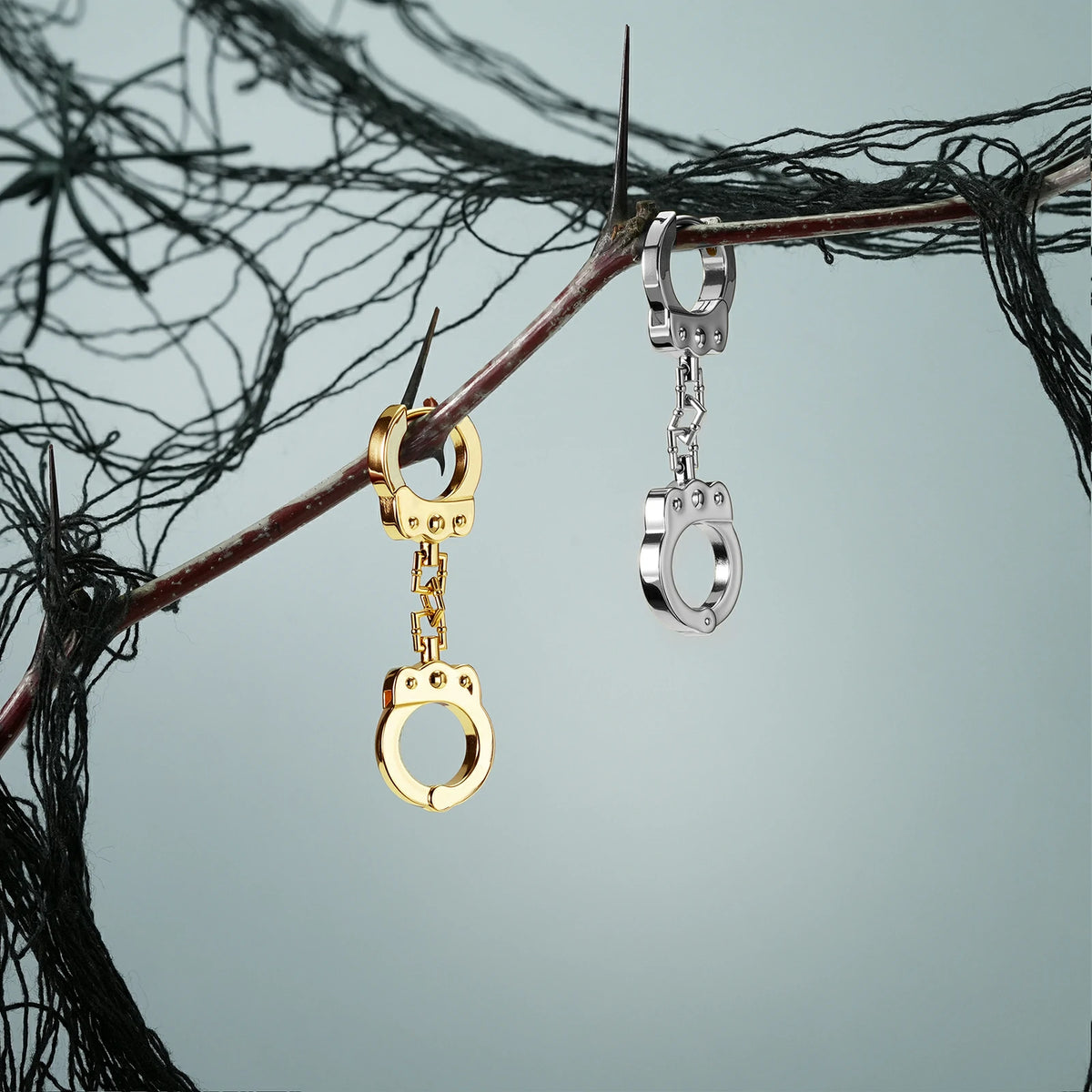 Gold and silver Handcuff Chain earrings hanging from a dark branch