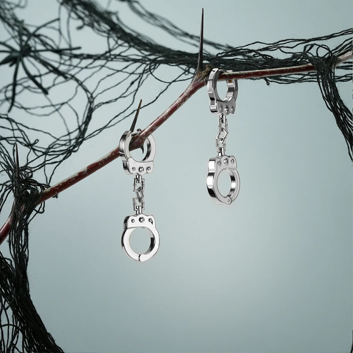 Pair of silver Handcuff Chain earrings hanging from a dark branch