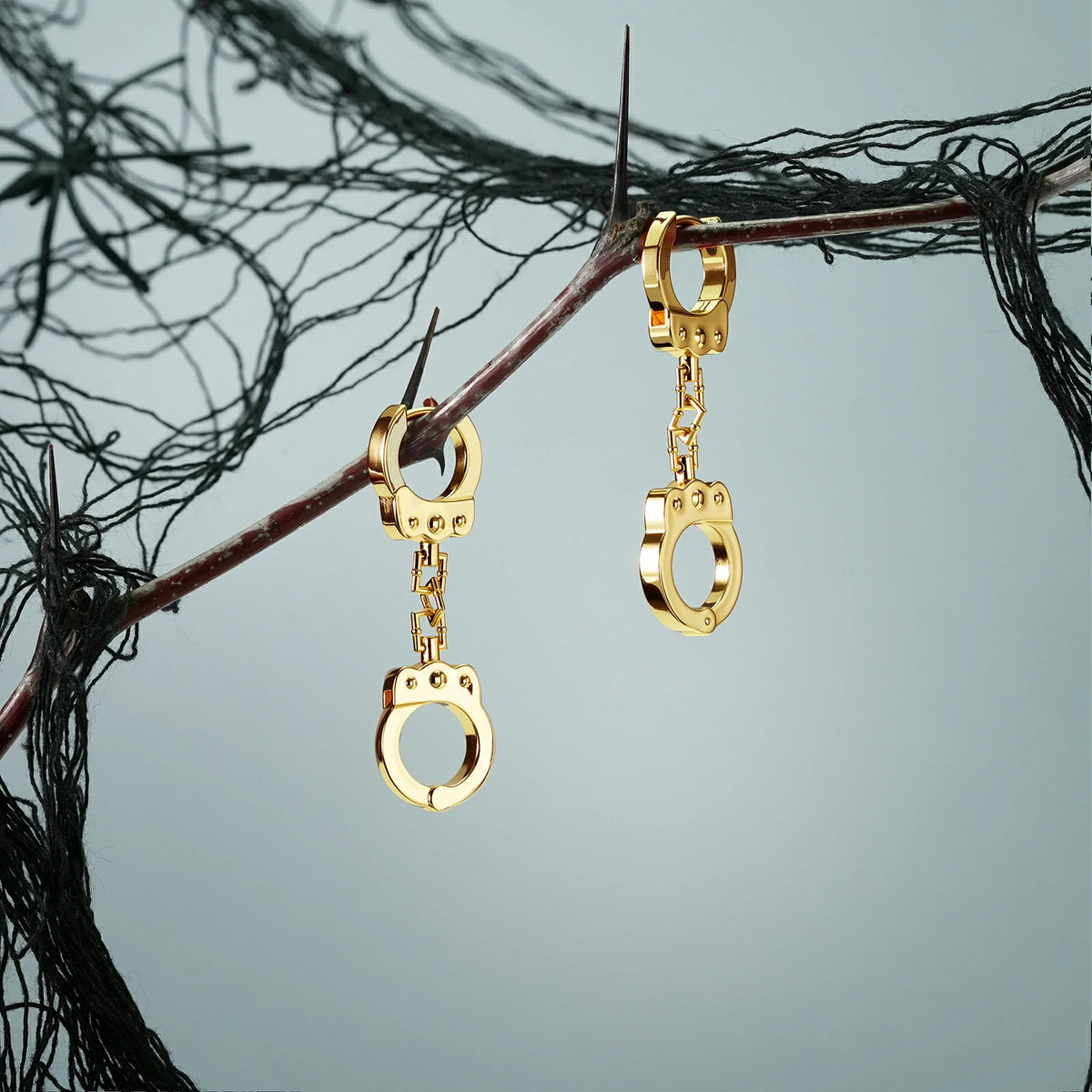 Pair of gold Handcuff Chain earrings hanging from a dark branch