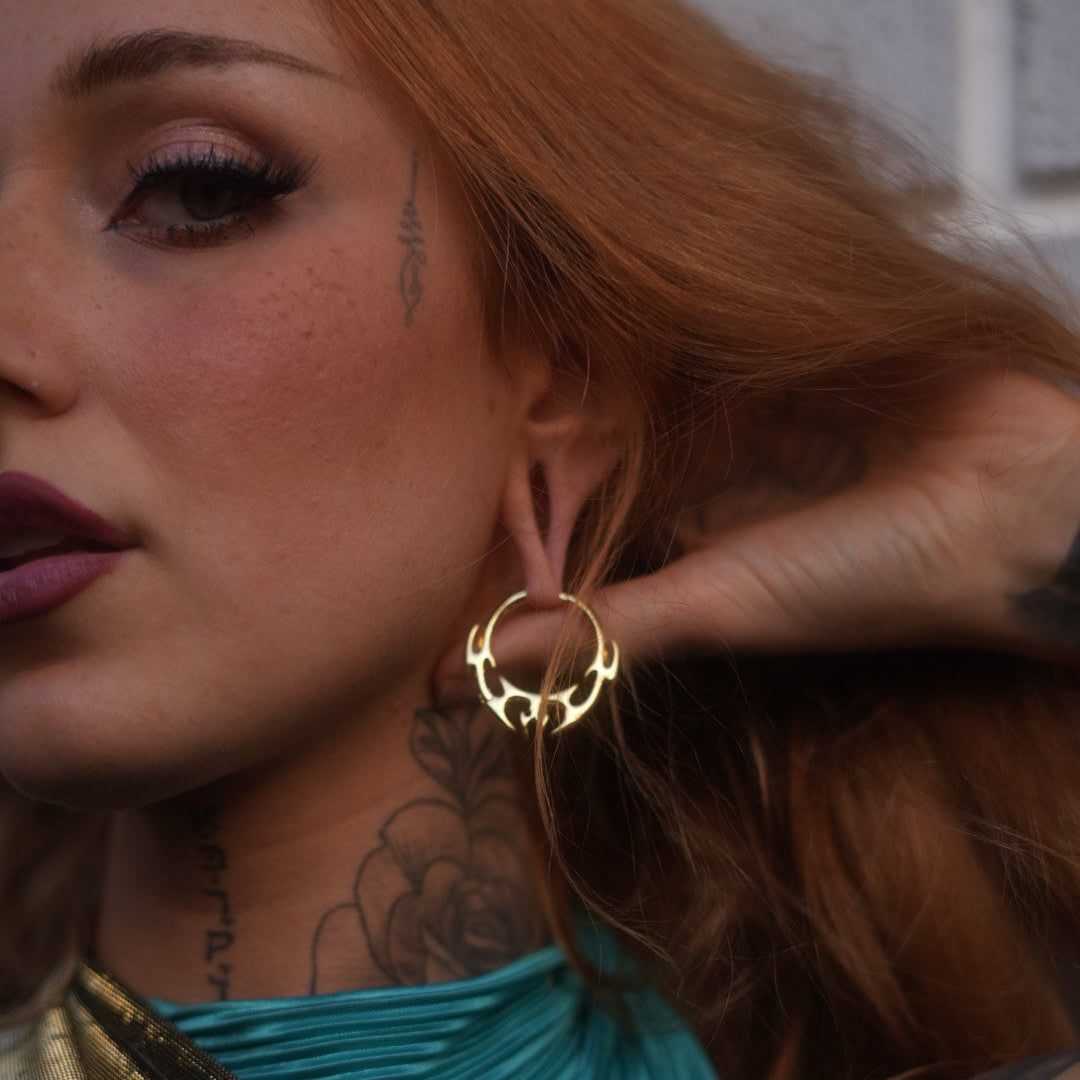 Close-up of a model with red hair wearing a gold-tone hoop earring with spiked wing design