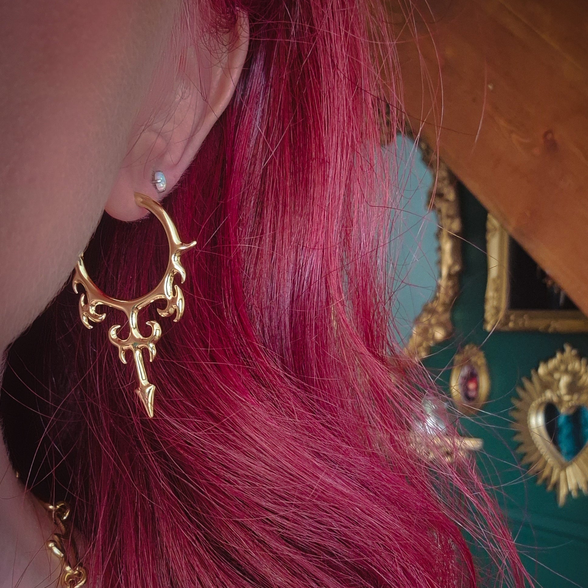 Close-up of gold Hellflame Blade hoop earring worn on the earlobe