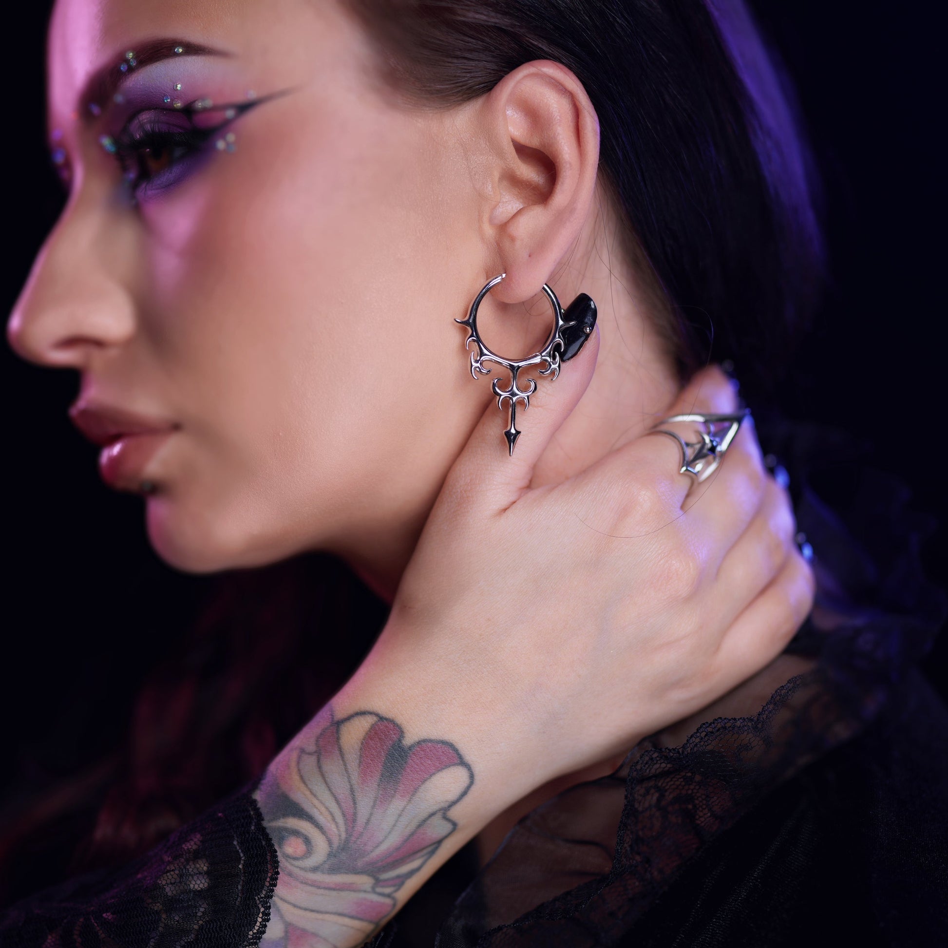 Silver-tone Hellflame Blade earrings worn in a layered ear styling look with multiple hoops and spikes