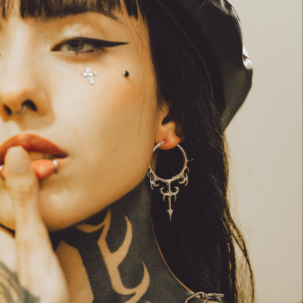 Silver-tone Hellflame Blade earring worn on a model, showing the ornate hoop and dagger drop from the side