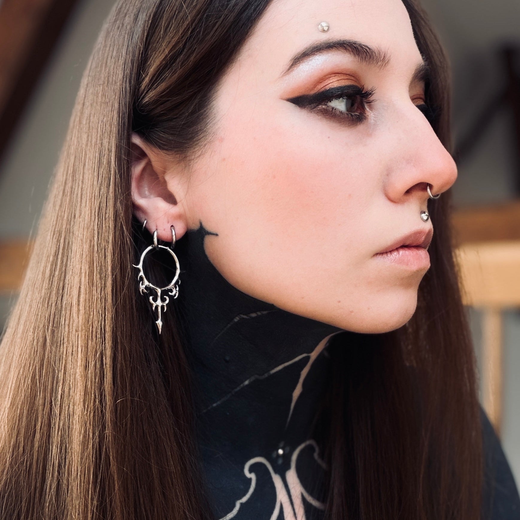 Silver-tone Hellflame Blade earring worn on a model, close side view of the flame scrollwork and pointed drop