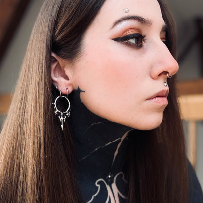 Silver-tone Hellflame Blade earring worn on a model, close side view of the flame scrollwork and pointed drop